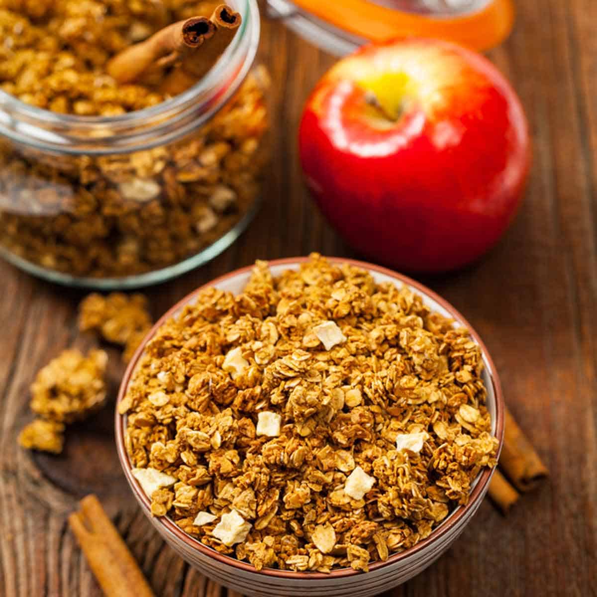 A bowl of apple granola with a fresh apple in the background.