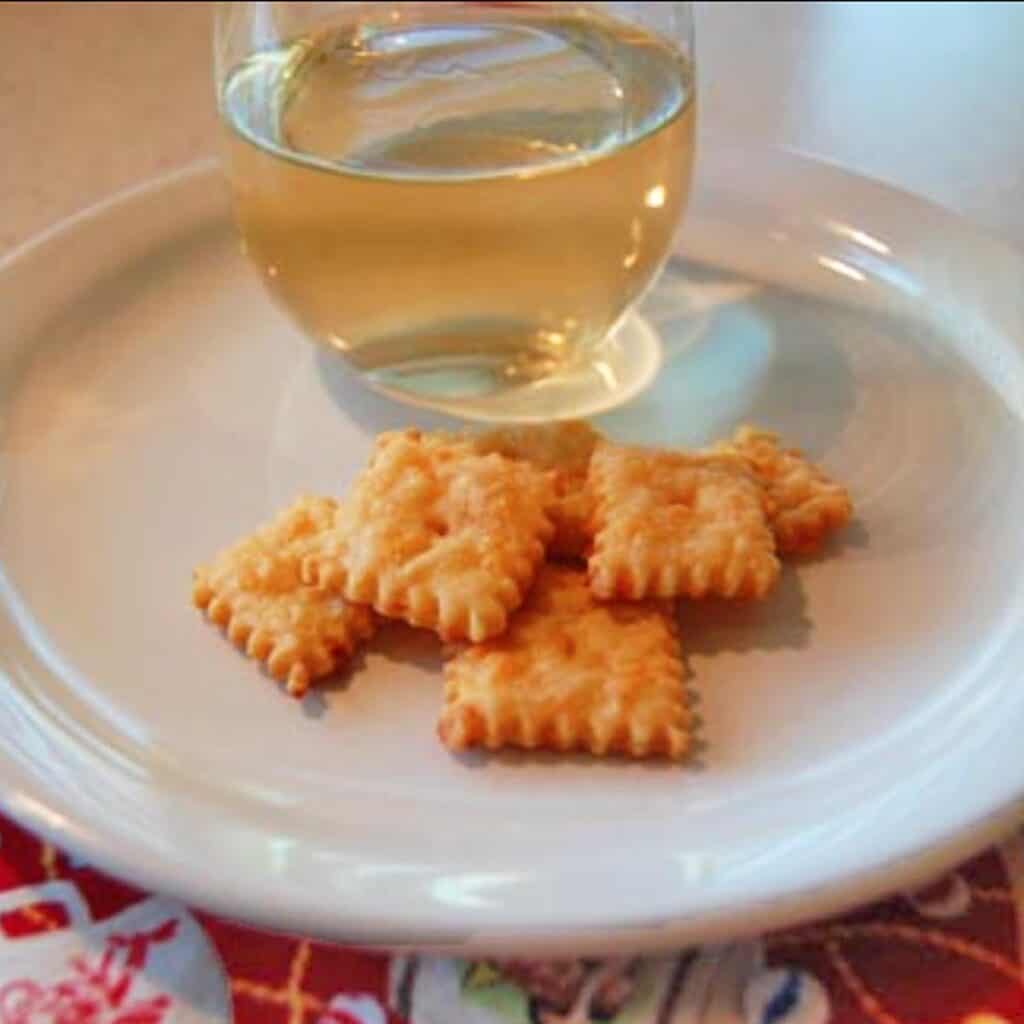6 homemade cheese crackers on a white plate with a glass of Chardonnay.