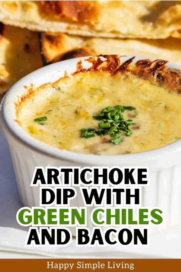 A bowl of artichoke dip with green chiles and bacon, garnished with chopped herbs, sits on a table. In the background, there are pieces of toasted bread. The text at the bottom reads, Artichoke Dip with Green Chiles and Bacon.