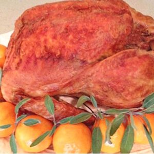Golden brown roast turkey on a platter surrounded by oranges and fresh sage leaves.
