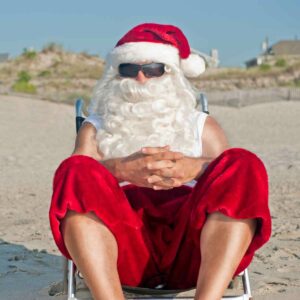 A man dressed in a Santa hat sitting on the beach.