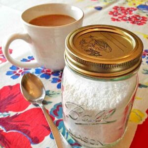 A jar of homemade sweetener with a cup of coffee in the background.