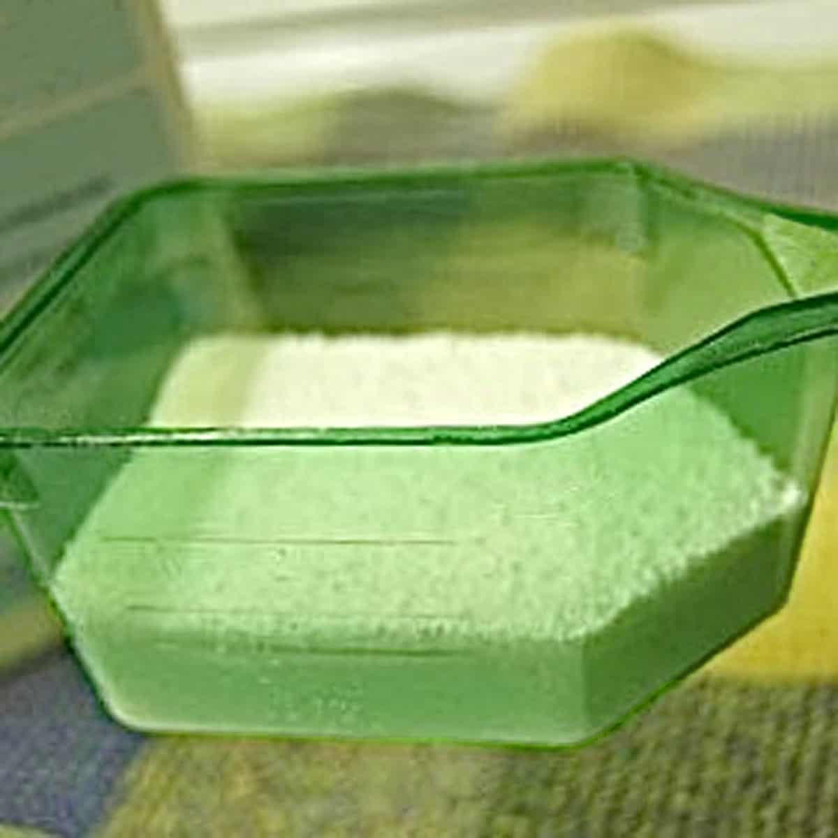 A green scoop partially filled with laundry detergent.