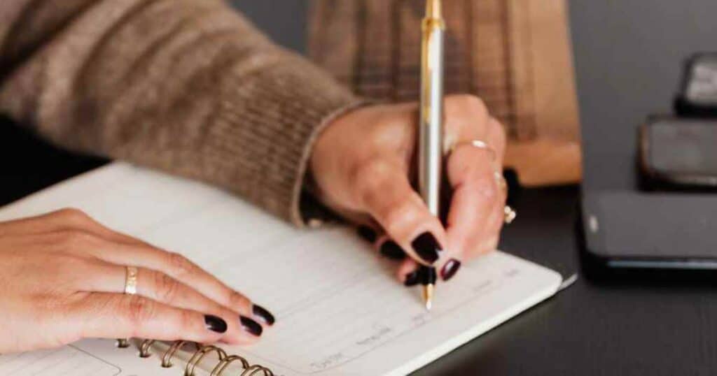 close up of a woman writing in a gratitude journal with a pen.