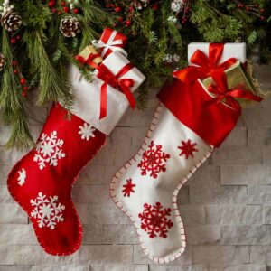 Two Christmas stockings hung on a mantel with greenery.