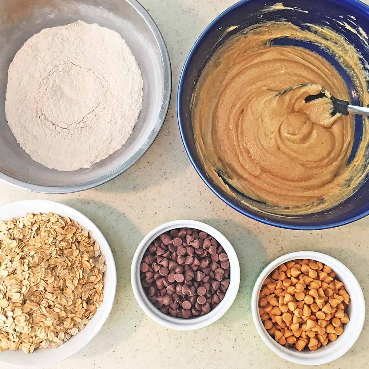 Five bowls containing the dry ingredients, wet ingredients, oatmeal, chocolate chips and butterscotch chips.