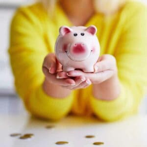 A woman in a yellow sweater holding a pink piggy bank.