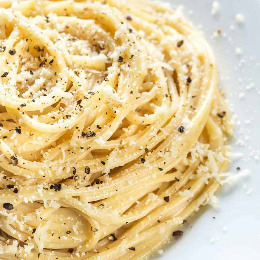 A white bowl of pasta noodles with Parmesan cheese and freshly ground black pepper.
