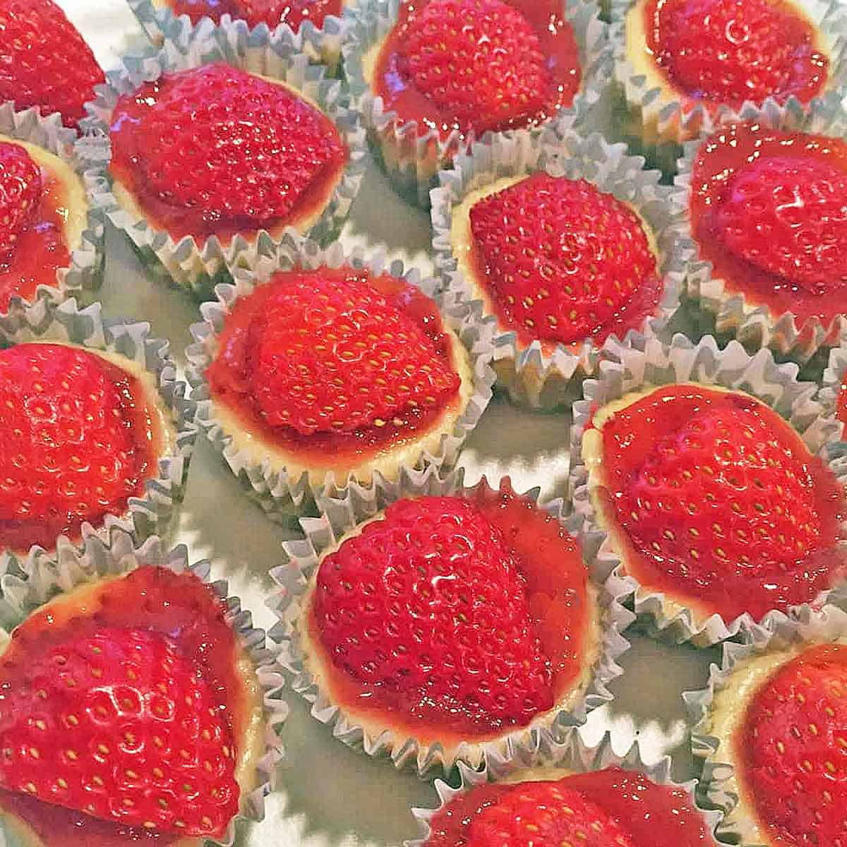 Mini strawberry cheesecakes topped with jam and a fresh berry.