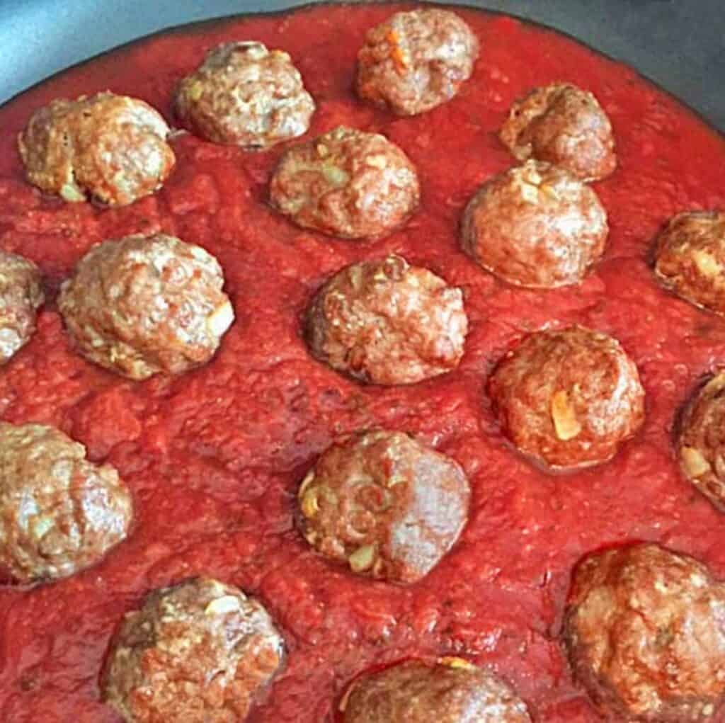 Homemade browned meatballs in a pot of spaghetti sauce.
