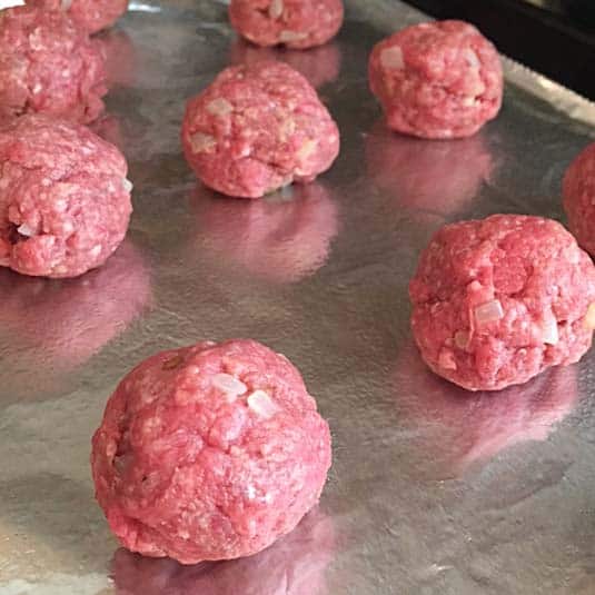Uncooked meatballs on a foil lined baking sheet.