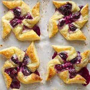 Four blackberry pinwheel pastries on a parchment lined baking sheet.