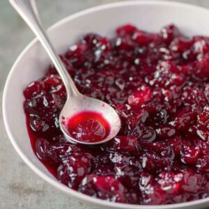 Ruby red whole berry cranberry sauce in a serving bowl with a silver serving spoon.