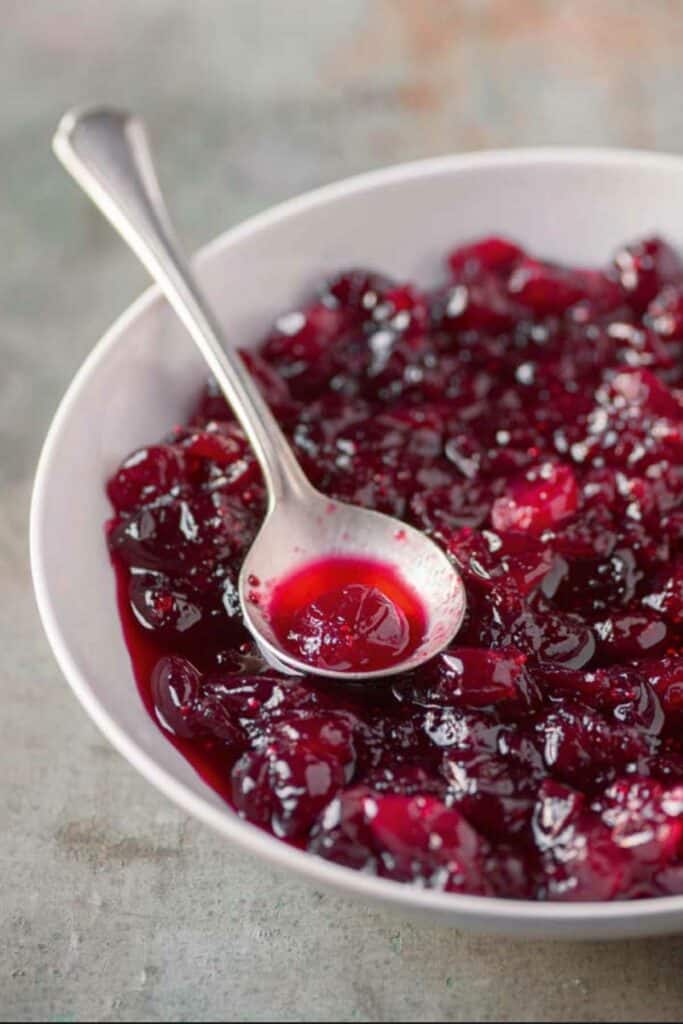 Homemade whole berry cranberry sauce in a white serving bowl with a spoon.