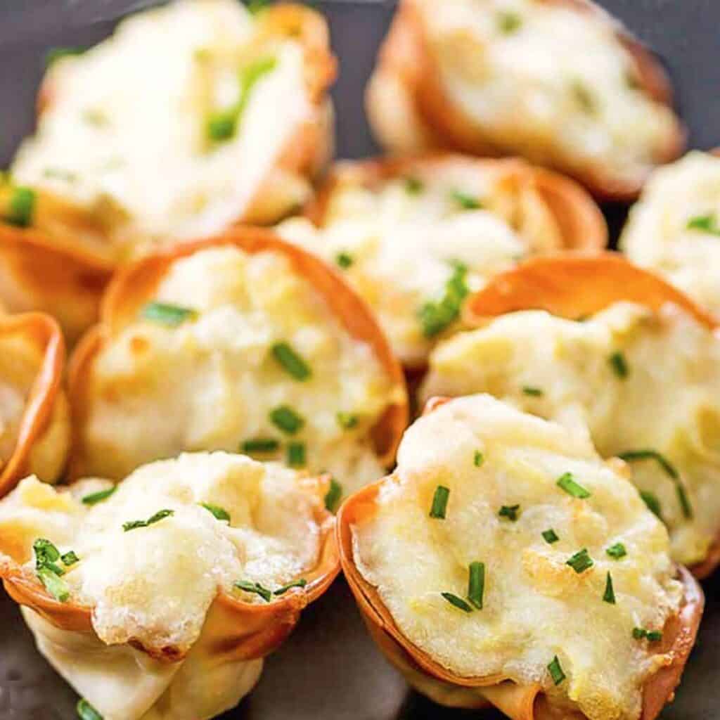 Crispy golden brown artichoke wonton wrappers with cheese on a serving plate.