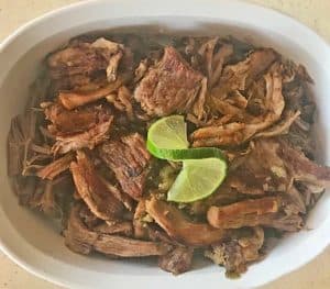 Pork Mexican Carnitas in a white serving dish with a fresh lime garnish.