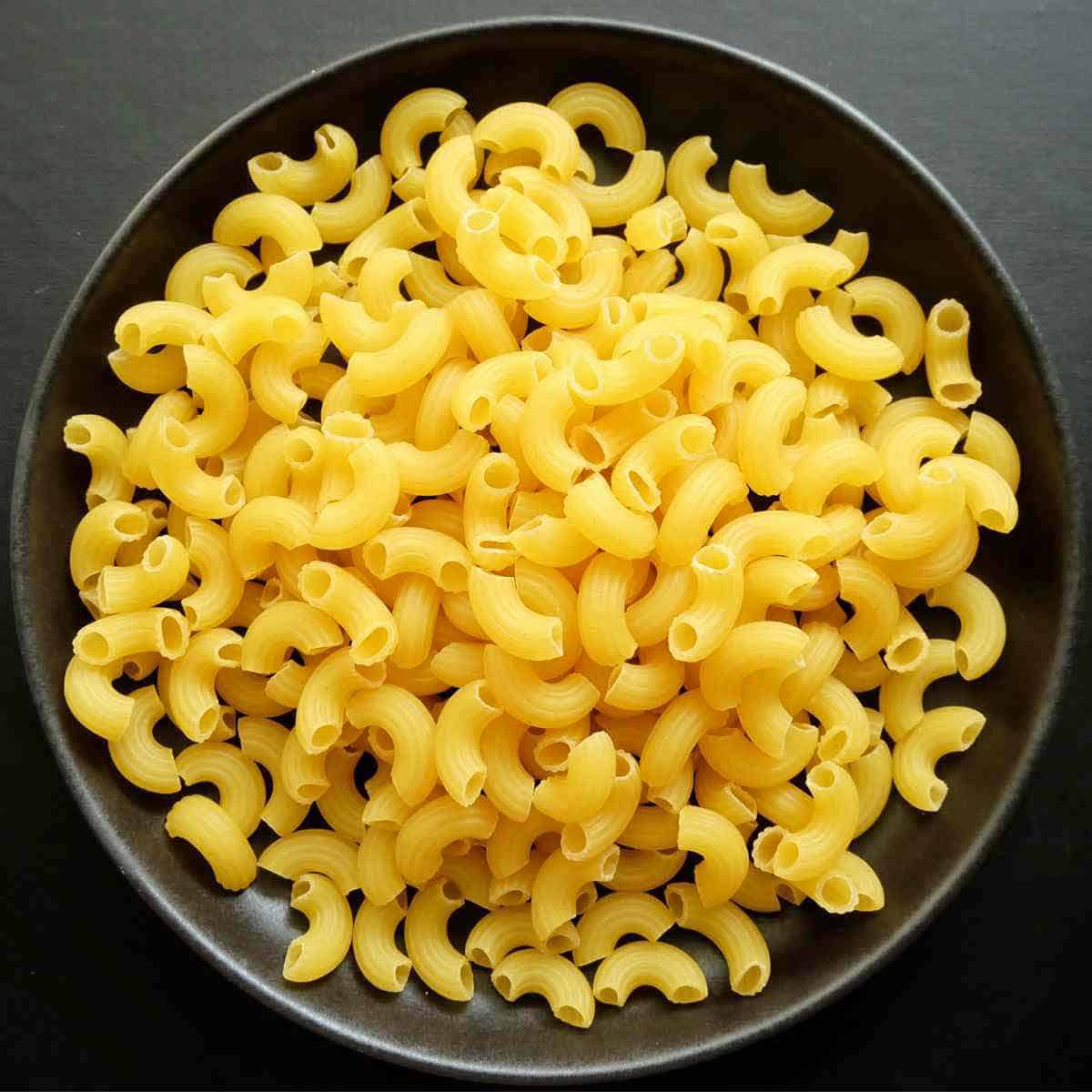 A black bowl of dry macaroni.