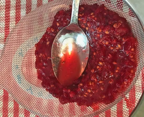 pressing red currants through a metal strainer with a spoon to extract the juice.