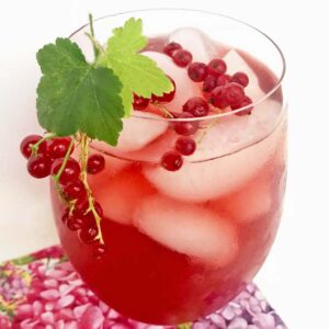 Red currant honey iced tea in a clear glass with fresh currants and red currant leaves.