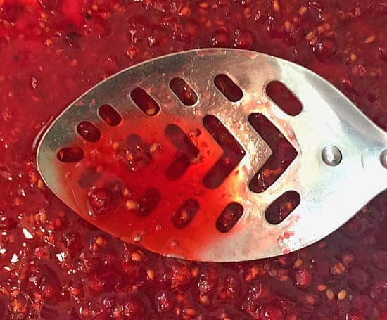crushing red currants with a metal spoon to extract the juice.