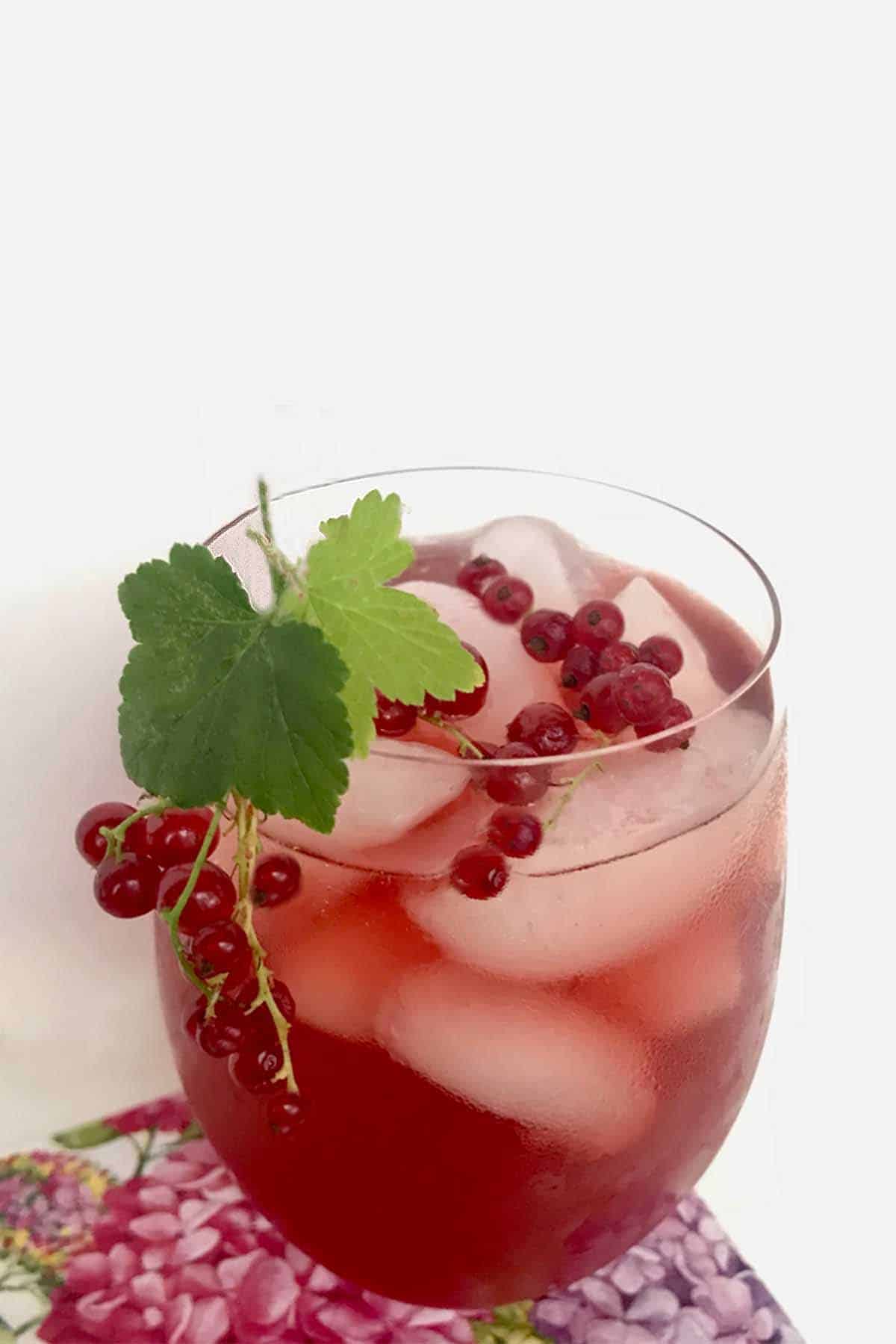 A glass of honey iced tea with red currants and currant leaves.