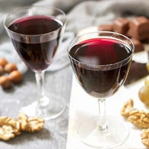 Two glasses of cassis on a table with walnuts and chocolate.