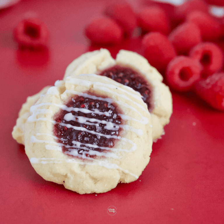 Raspberry Cheesecake Thumbprint Cookies on a red plate with raspberries in the background.
