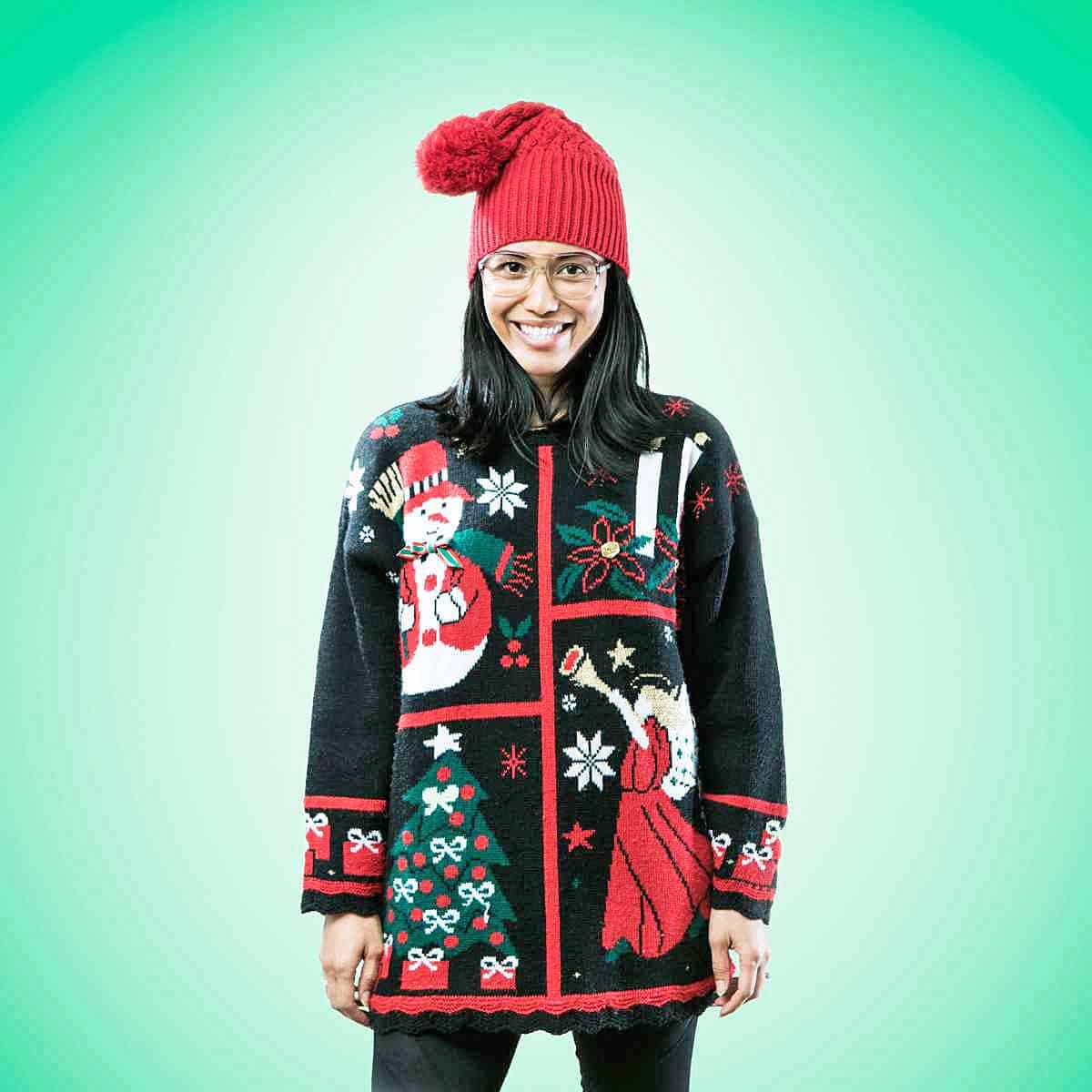 A woman wearing an ugly Christmas sweater and a red knit hat.