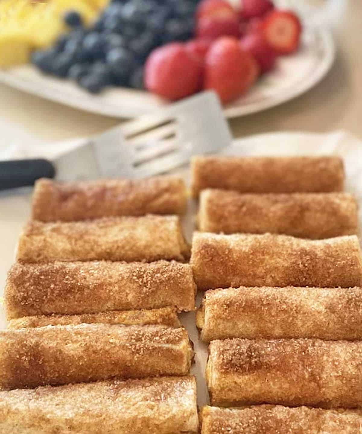 Ten cream cheese roll ups on a serving tray with fresh fruit in the background.