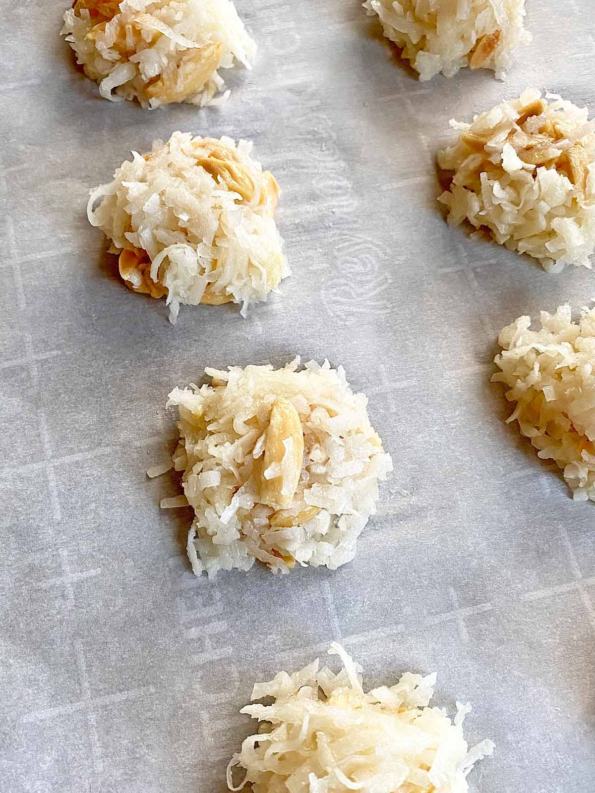 Unbaked balls of coconut macaroon dough on a parchment lined baking sheet.