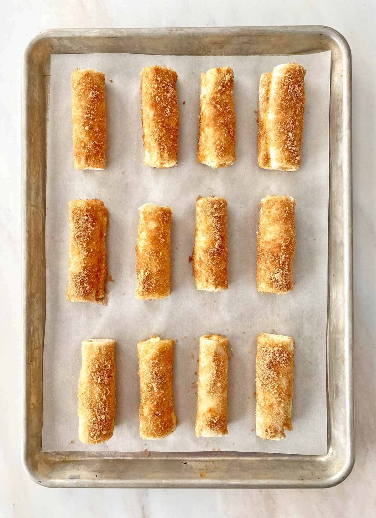 Unbaked breakfast roll ups on a parchment paper lined baking sheet.