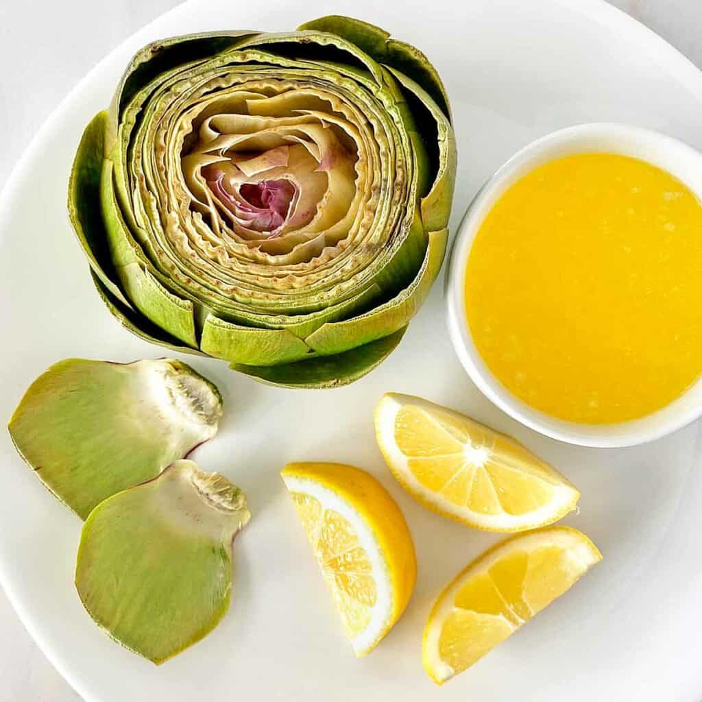 A microwave steamed artichoke ready for serving with lemon wedges and melted butter.