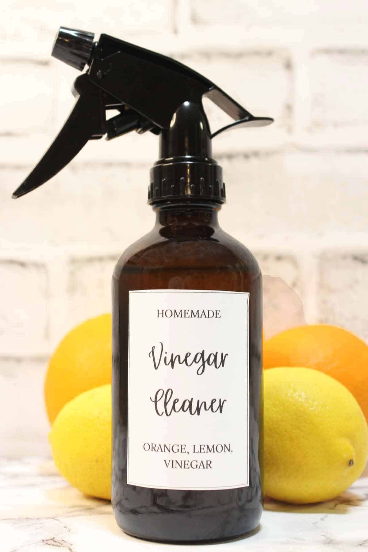 Spray bottle of DIY orange and lemon peel cleaner on a counter with oranges and lemons.