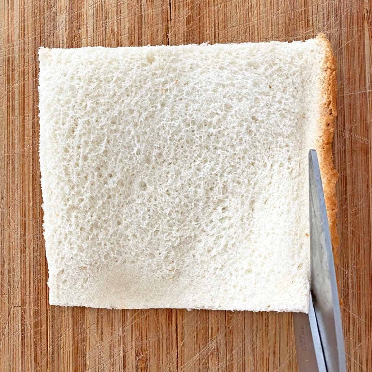 Cutting crusts off a flattened piece of bread with kitchen scissors.