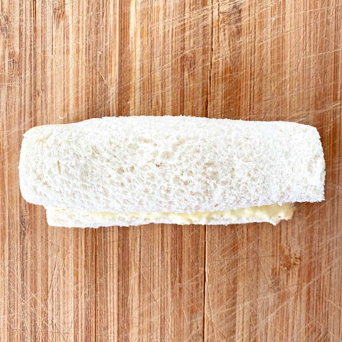 A trimmed bread slice wrapped around cream cheese filling in a roll shape.