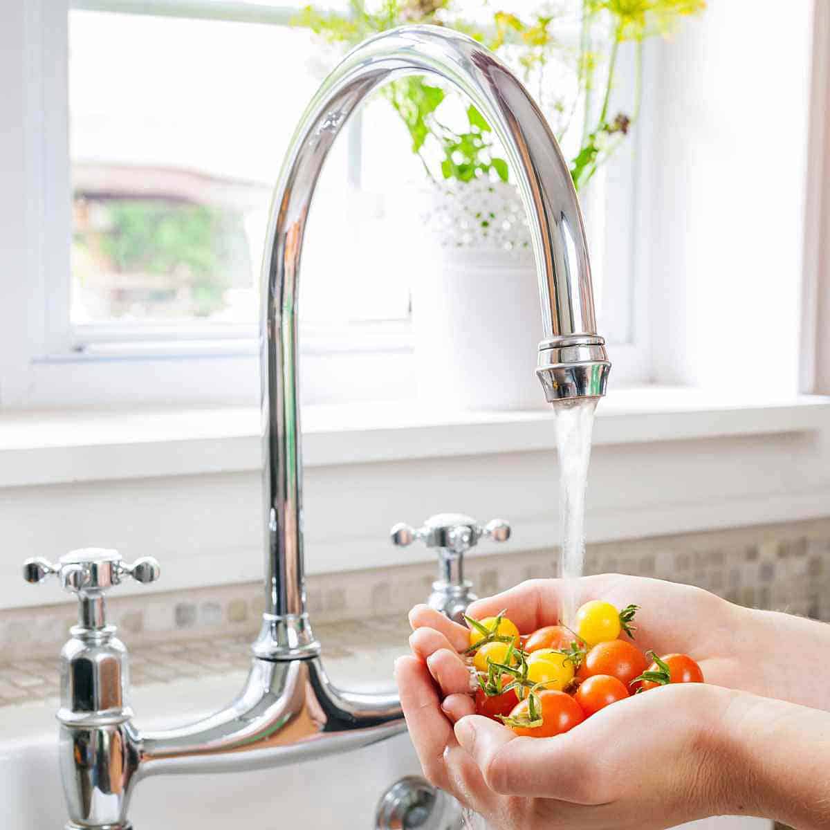 Washing cherry tomatoes under running water in a kitchen sink.