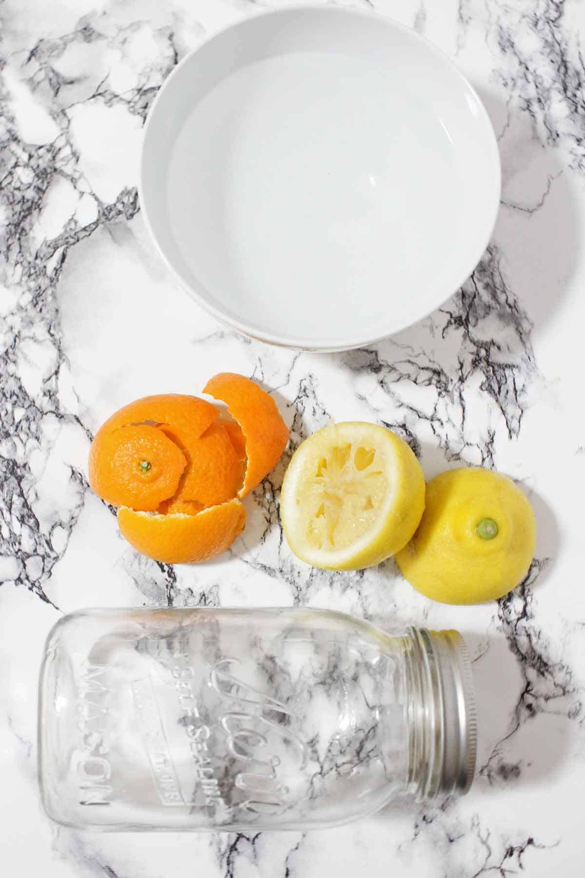 Orange peelings, lemon peels, a jar, and a bowl of white vinegar.