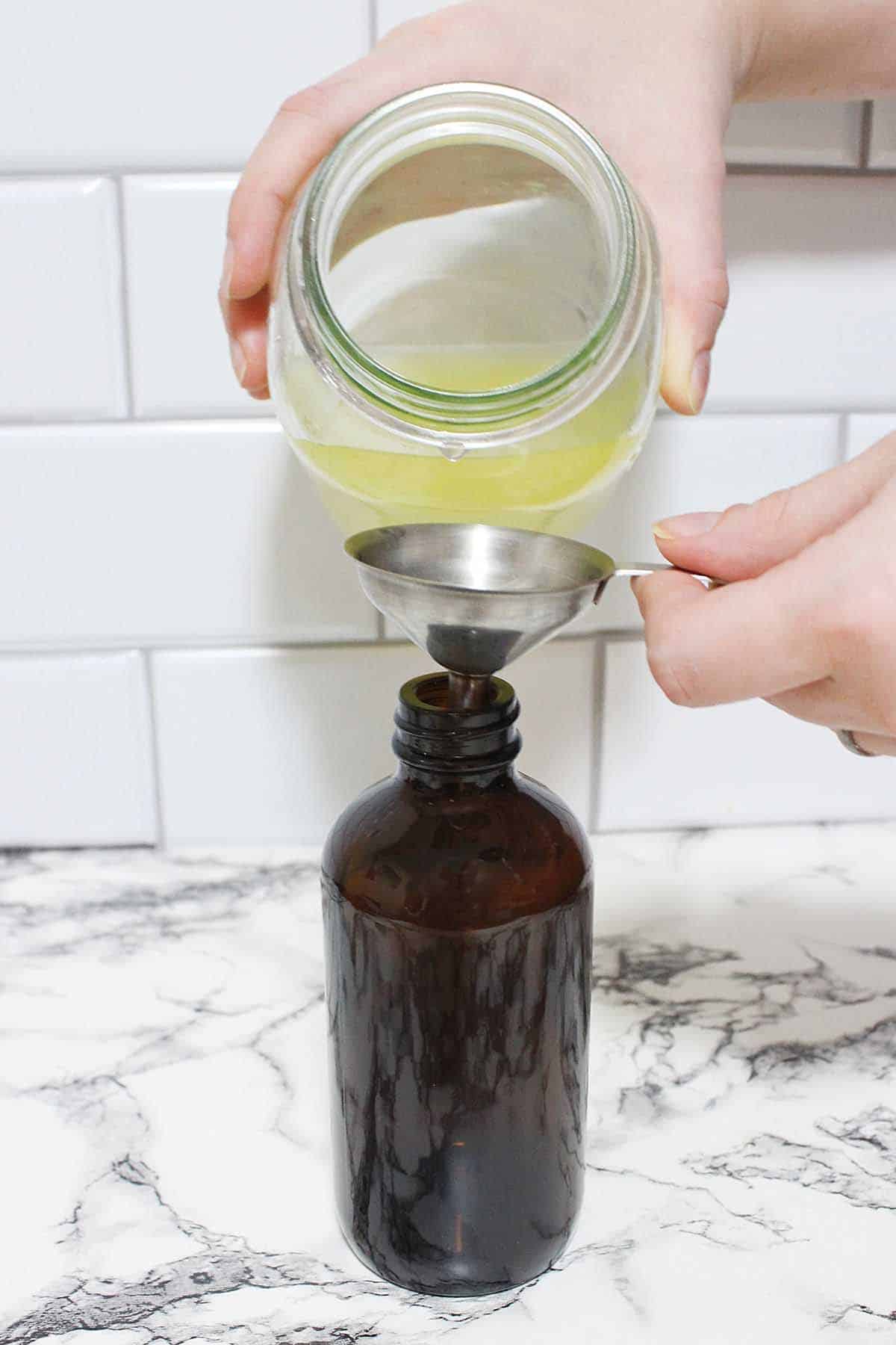 Pouring homemade orange lemon cleaner into a spray bottle with a funnel.