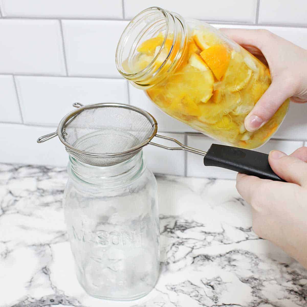 Straining the orange and lemon peel vinegar mixture into a clean jar.
