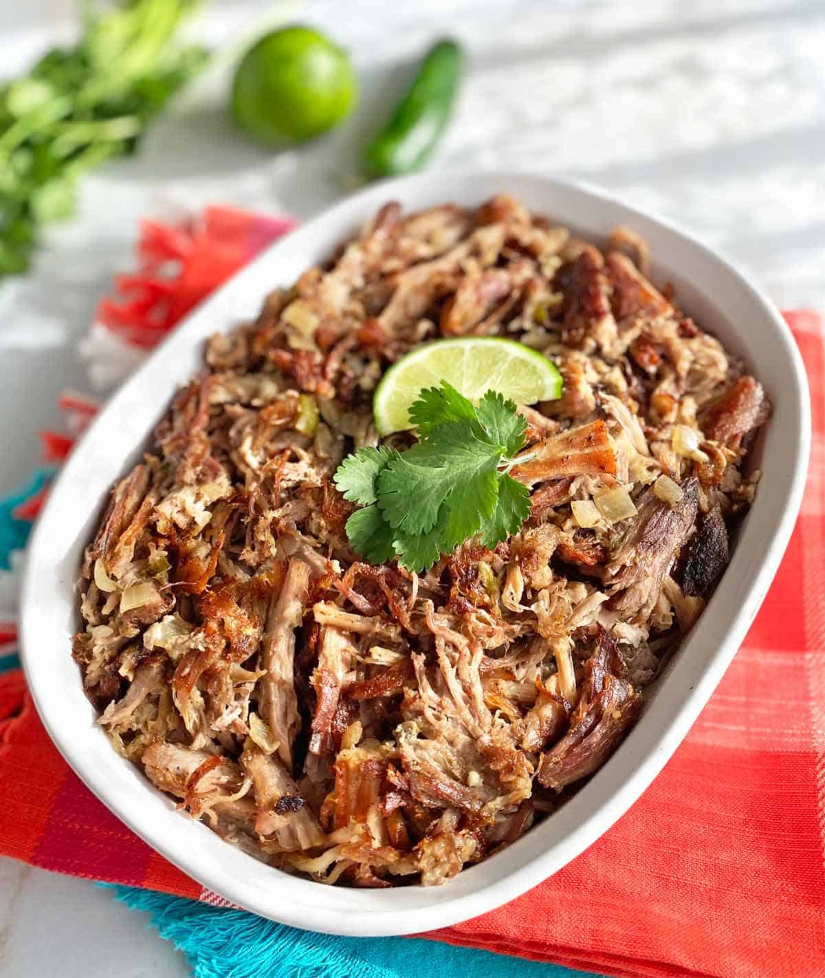 Mexican Carnitas cooked in the crock pot in a serving dish atop bright colored napkins.