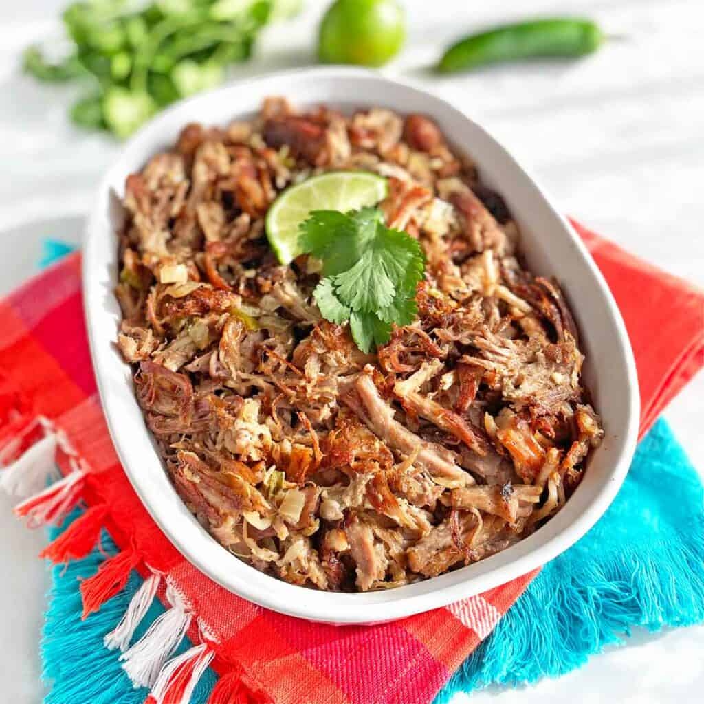 Finished Mexican Carnitas in a white serving dish on colorful napkins.