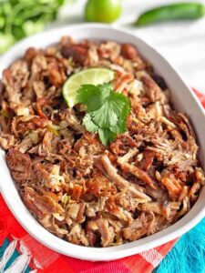 Mexican Carnitas shredded pork in a serving dish with limes and cilantro.
