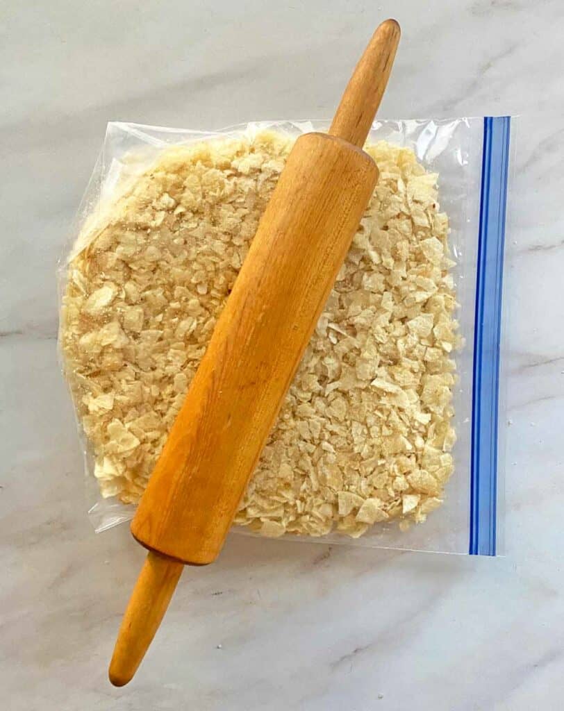 Crushing potato chips in a zip lock bag with a rolling pin.