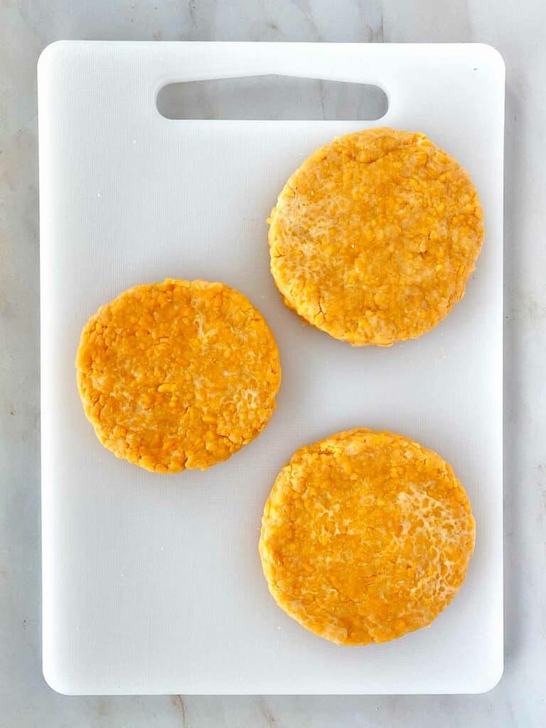 Three discs of chilled cheese cracker dough on a cutting board.