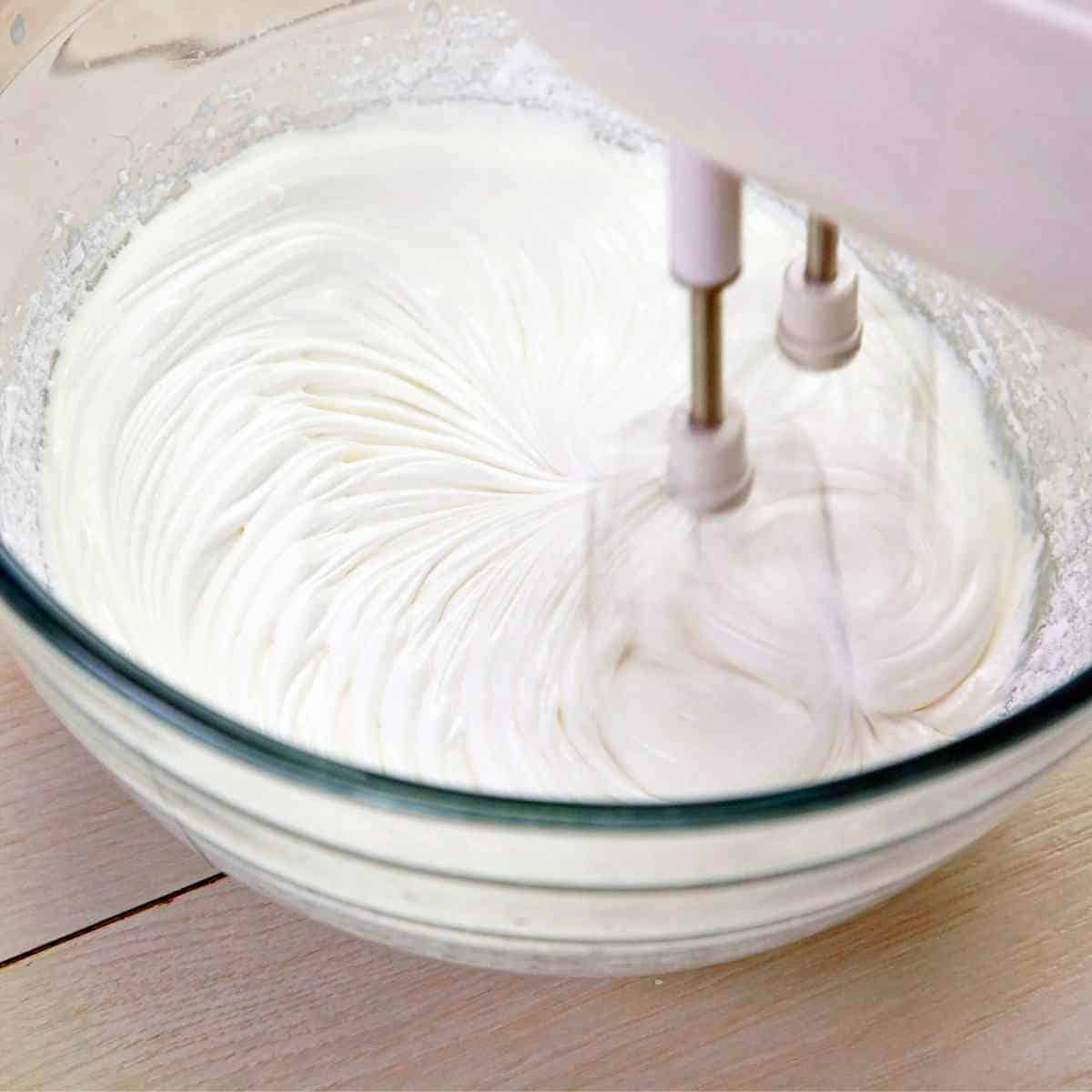 An electric mixer beating whipped cream in a bowl.