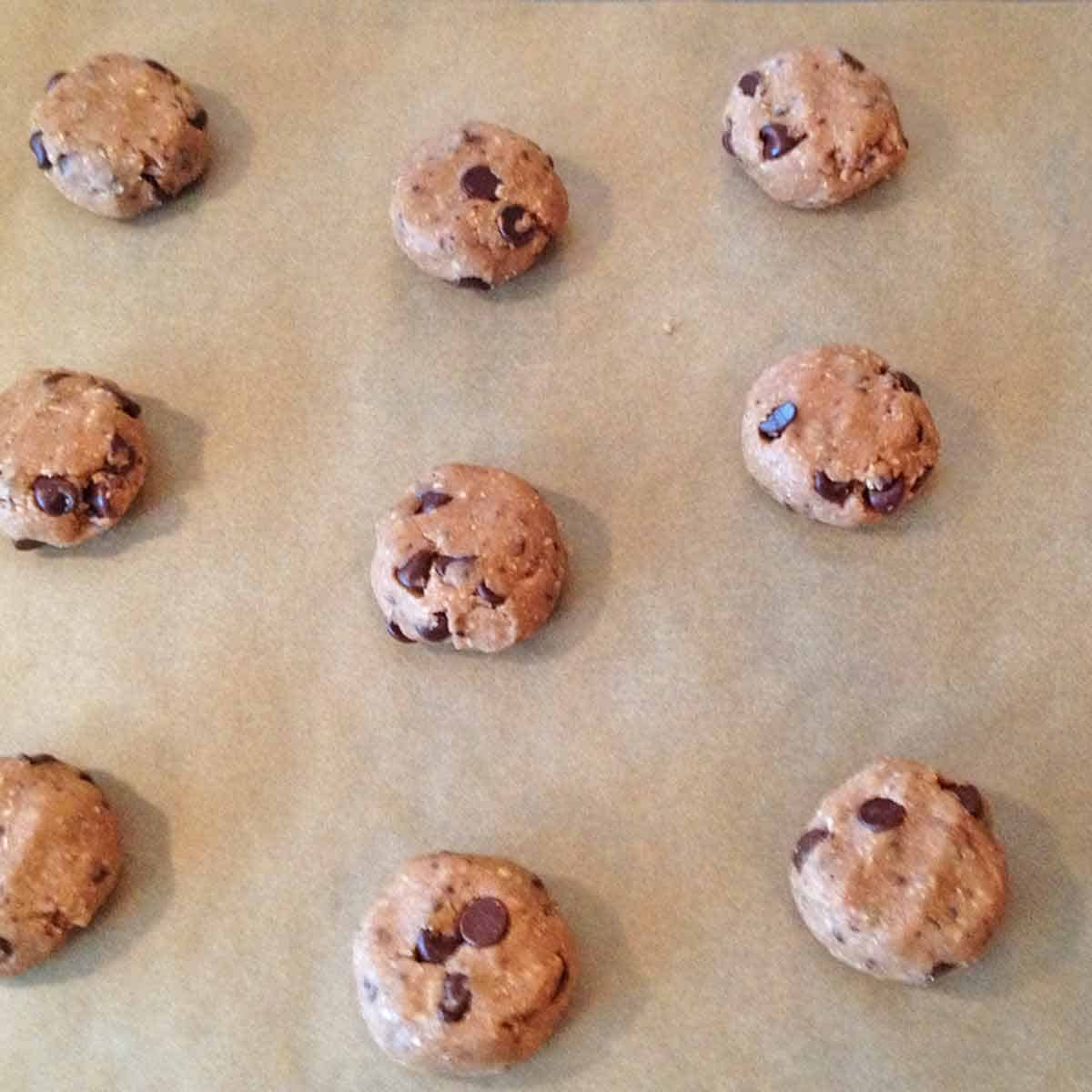 Flattened chocolate chip cookie balls on a baking sheet ready to cook in the oven.