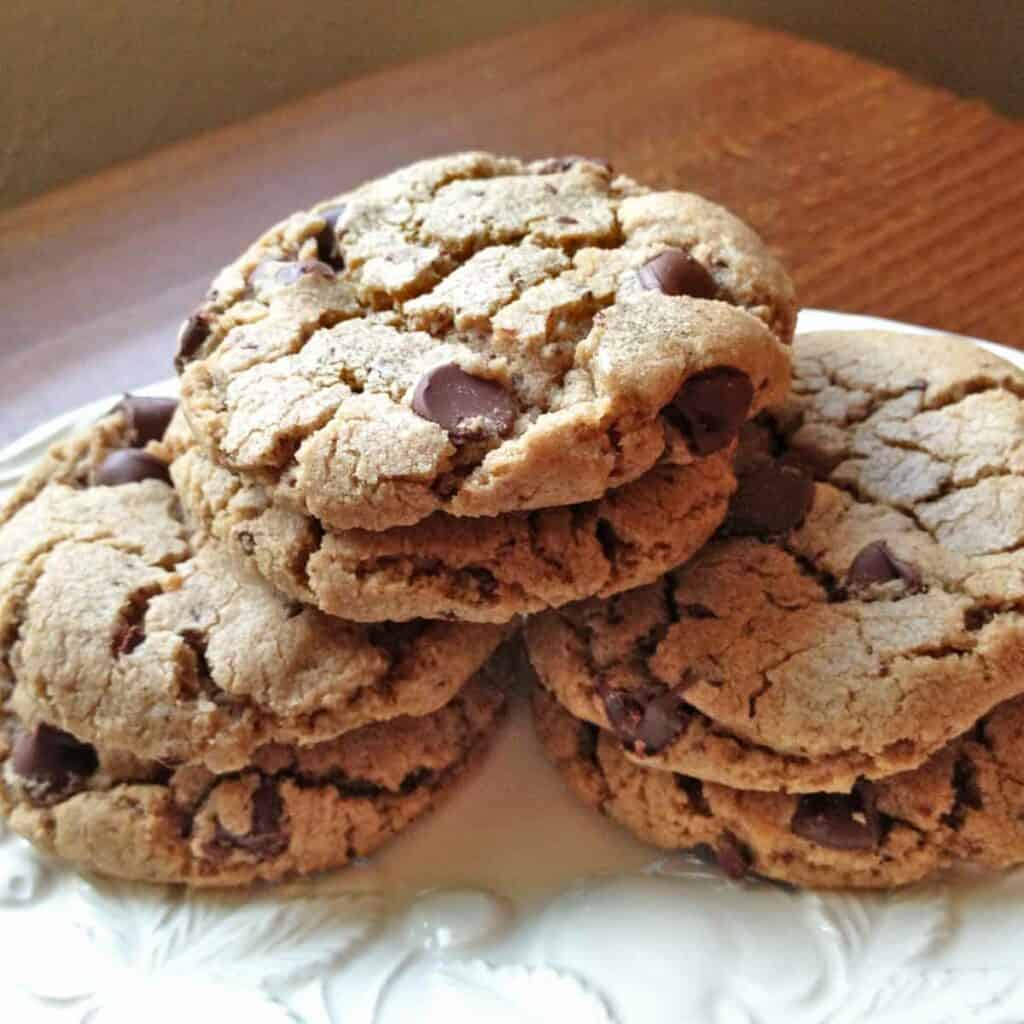 Six baked soft chocolate chip cookies with sea salt on a white serving dish.