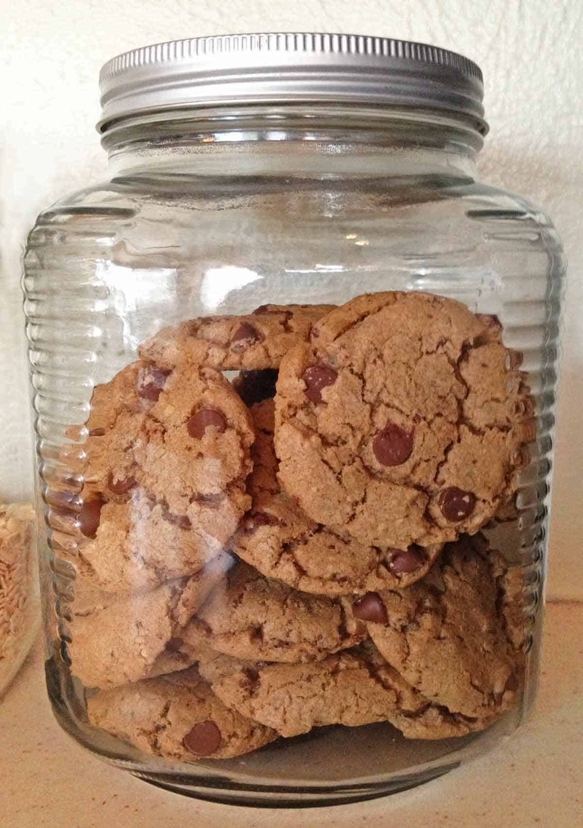 A glass cookie jar filled with sweet and salty chocolate chip cookies.