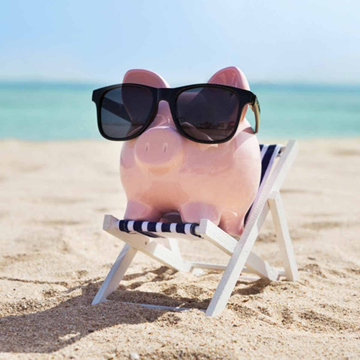 A pink piggy bank wearing sunglasses and relaxing on the beach.
