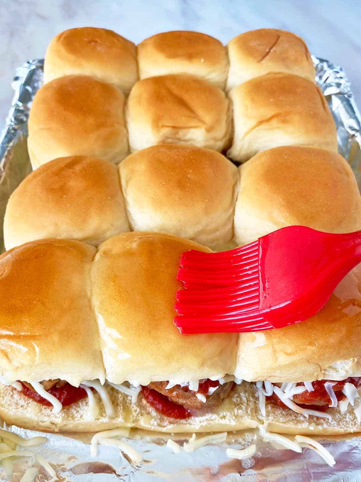 Brushing unbaked sliders with garlic butter using a red silicone brush.